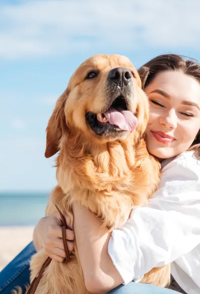 Dog and woman sitting on the beach hugging. 